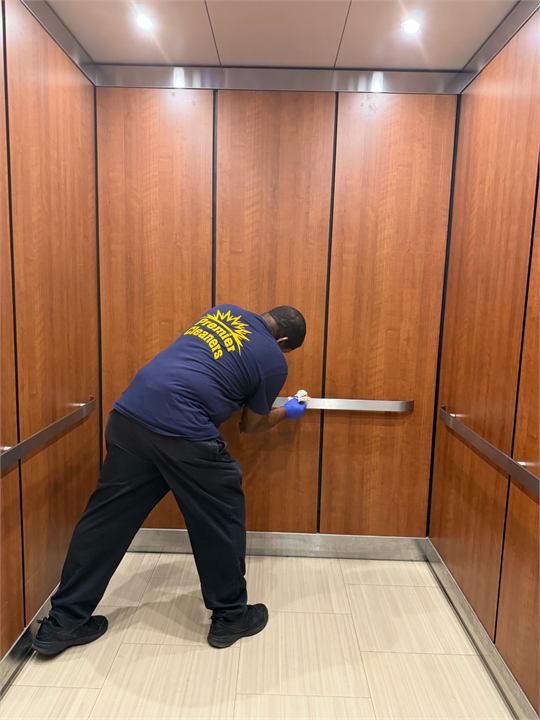 Premier worker cleaning an elevator handrail in a commercial interior.