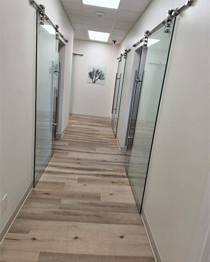 Clean commercial hallway with light walls, glass doors, and wood-look flooring.